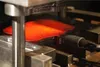 A close-up view of a hot, glowing piece of metal being shaped by machinery. Produktbild-Vorschau