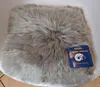 A fluffy gray sheepskin seat cushion is placed on a white chair, with a blue product tag attached to the corner. Produktbild-Vorschau