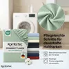 A folded green fitted sheet with a close-up view of its texture, a stack of fitted sheets in various colors, a washing machine in the background, and care instructions. Produktbild-Vorschau