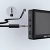 A close-up view of a black electronic device with several ports, and a microphone cable with a 3.5mm jack being inserted into one of the ports. A magnified view of the jack is shown in a circle. Náhled obrázku produktu