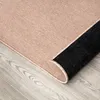A close-up view of a rug with a beige top and a black underside, partially rolled up, on a light gray wooden floor. Produktbild-Vorschau