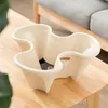 A cream-colored, multi-tiered planter sits on a wooden table, with a blurred background of a couch and wooden furniture. Voir les images du produit
