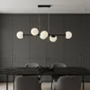 A modern black chandelier with six white glass globe lights hangs above a black marble dining table with gray chairs. Produktbild-Vorschau