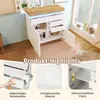 A white sideboard with a wood-effect top, featuring open doors and drawers, set in a well-lit room with a window and wooden flooring. Below the main image are three smaller images highlighting product features. Podgląd zdjęcia produktu