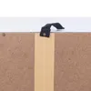 A close-up view of the top edge of a particleboard panel, showing a black fabric handle attached with a metal rivet and a strip of brown paper tape. Produktbild-Vorschau