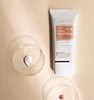 A tube of GUINOT Youth Perfect Finish Cream with SPF 50 is shown next to a petri dish containing a dollop of the cream. Produktbild-Vorschau