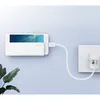 A white smartphone wall mount is attached to a wall, holding a smartphone that is charging via a white cable connected to a white wall charger. Produktbild-Vorschau