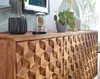 A close-up view of a wooden sideboard with a geometric carved pattern on its doors, decorated with potted plants and a glass dome object. Náhled obrázku produktu
