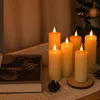 A group of LED candles are arranged on a table with a book and pinecones, with a decorated Christmas tree in the background. Voir les images du produit