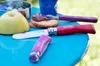 A close-up of Opinel knives and an apple on a blue table outdoors. Produktbild-Vorschau