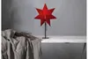 A red star-shaped lamp sits on a white table next to a draped grey cloth and some dried branches. Podgląd zdjęcia produktu