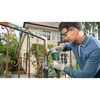 A man is using an angle grinder to clean a rusty metal gate in front of a house. Produktbild-Vorschau