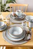 A table setting with plates, bowls, mugs, and cutlery, arranged on placemats. Produktbild-Vorschau