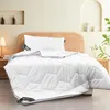 A white comforter with a hexagonal pattern is laid out on a bed with a woven headboard. A white pillow is placed on top of the comforter. Produktbild-Vorschau