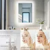 A bathroom mirror with integrated LED lighting, featuring a smart touch sensing function and anti-fog capabilities, shown in a lifestyle setting with a woman applying skincare. Náhľad obrázku produktu