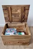 An open wooden chest with a lid, containing a puzzle box and sunglasses. Produktbild-Vorschau