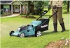 A person is mowing a lawn with a Makita lawnmower in front of a house. Náhled obrázku produktu