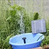 A solar-powered water pump kit is set up in a garden, with water spraying from a small fountain head into a blue basin. Podgląd zdjęcia produktu