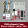 A collection of model building kit components, including a truck chassis, body parts, wheels, decals, instructions, and background scenery pieces, laid out on a gray surface. Produktbild-Vorschau