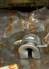 A metal part is shown in focus against a blurred background of plastic packaging. Produktbild-Vorschau