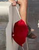 A person is sitting on a ledge, holding a red drawstring bag. Produktbild-Vorschau