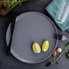 A gray plate with two lime wedges, a black knife, a fork, a glass of water, garlic, and a small plant on a dark gray surface. Náhled obrázku produktu