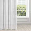 A white sheer curtain hangs in front of a window with a view of green trees. Produktbild-Vorschau