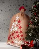 A large burlap sack with red and white stars and the words "Merry Christmas" is placed next to a decorated Christmas tree. Produktbild-Vorschau