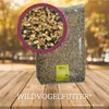 A large bag of wild bird food is displayed on a wooden surface with a close-up inset of the bird seed mix. The background is blurred with autumn foliage. Produktbild-Vorschau