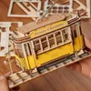 A person's hands are holding a wooden 3D puzzle model of a tram. Produktbild-Vorschau