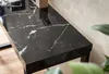 A close-up of a black marble-look console table with white veining, placed against a textured wall. A plant is visible in the foreground. Produktbild-Vorschau