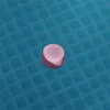 A small, pink, round Bluetooth speaker floats on the surface of a blue, grid-patterned pool. Náhľad obrázku produktu