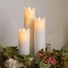 Three LED candles of varying heights are arranged in a decorative floral arrangement. Produktbild-Vorschau