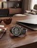 A watch, sunglasses, and a wallet are placed on a wooden desk next to a laptop. A cat is visible in the background. Anteprima dell’immagine prodotto