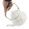 A hand holding a white and gold marble-patterned teapot. Podgląd zdjęcia produktu