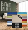 A stack of colorful fitted sheets is displayed on a wooden surface in front of a bedroom scene with a large logo on the wall. Produktbild-Vorschau