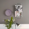 A wall with a clock, magazine rack, and flowers. Náhľad obrázku produktu