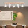 A modern wooden ceiling light fixture with five white spotlights is shown above a dining table setting. Produktbild-Vorschau