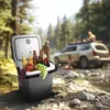 A portable cooler filled with drinks and fruit sits on a rocky riverbank, with people and a car in the background. Podgląd zdjęcia produktu