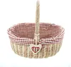 A woven basket with a red and white checkered lining and a heart-shaped charm. Produktbild-Vorschau