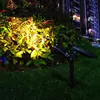 A solar-powered garden spotlight illuminates plants at night, with a building in the background. Voir les images du produit
