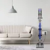 A Dyson vacuum cleaner and its accessories are neatly organized on a stand next to a sofa in a living room. Produktbild-Vorschau