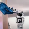 A blue-gloved hand holds a smartphone over a small, silver robot figurine. Voir les images du produit