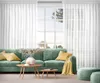 A living room scene with a green sofa, coffee tables, and white curtains. Produktbild-Vorschau