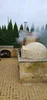 An outdoor scene with a smoking pizza oven and a wood storage area. Náhled obrázku produktu
