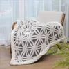 A soft, patterned blanket draped over a chair in a room with sheer curtains. Produktbild-Vorschau