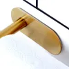 A close-up shot of a gold toilet paper holder attached to a white tiled wall, with a roll of toilet paper on it. Produktbild-Vorschau