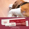 A dog is lying down with a product tube and box in the foreground. Produktbild-Vorschau