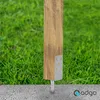 A wooden post with a metal bracket is anchored into the ground next to a concrete path, with grass in the background. Náhled obrázku produktu
