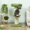 A cat sits on a green cat tree next to a plant stand and a bowl of food. Produktbild-Vorschau
